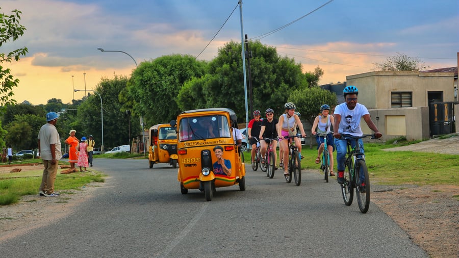 Group riding bikes alongside tuk tuk in Soweto