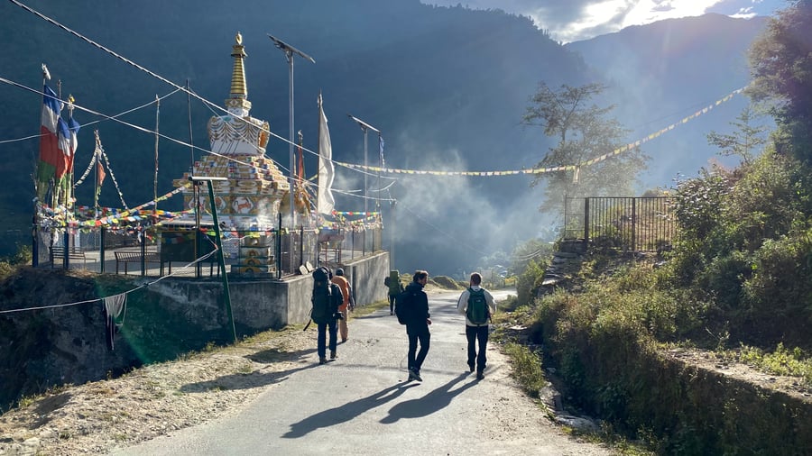 Travellers hiking past a Stupa with prayer flags