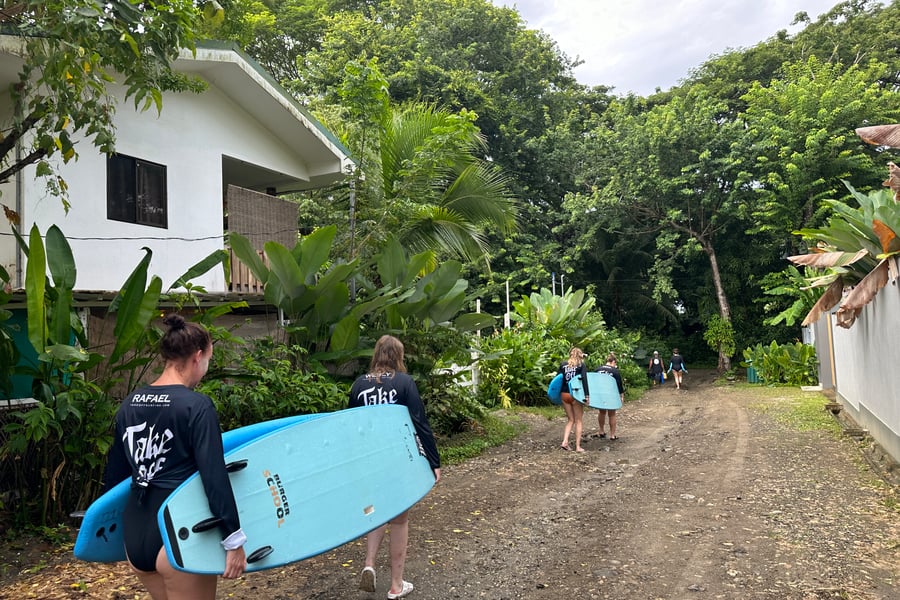 Meiden dragen surfboards over een lokale weg